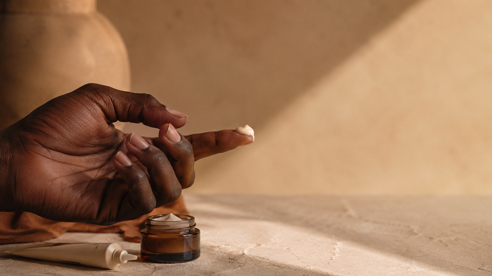 A Black hand applying a small measured amount of cream to a fingertip