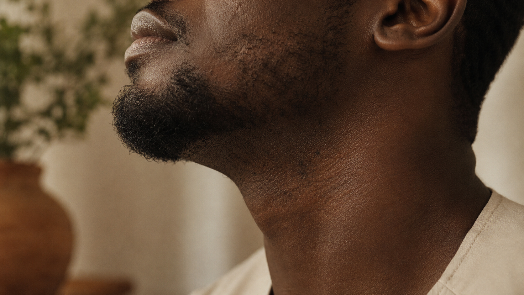 A young man's jaw and beard line on deep brown skin, soft warm light