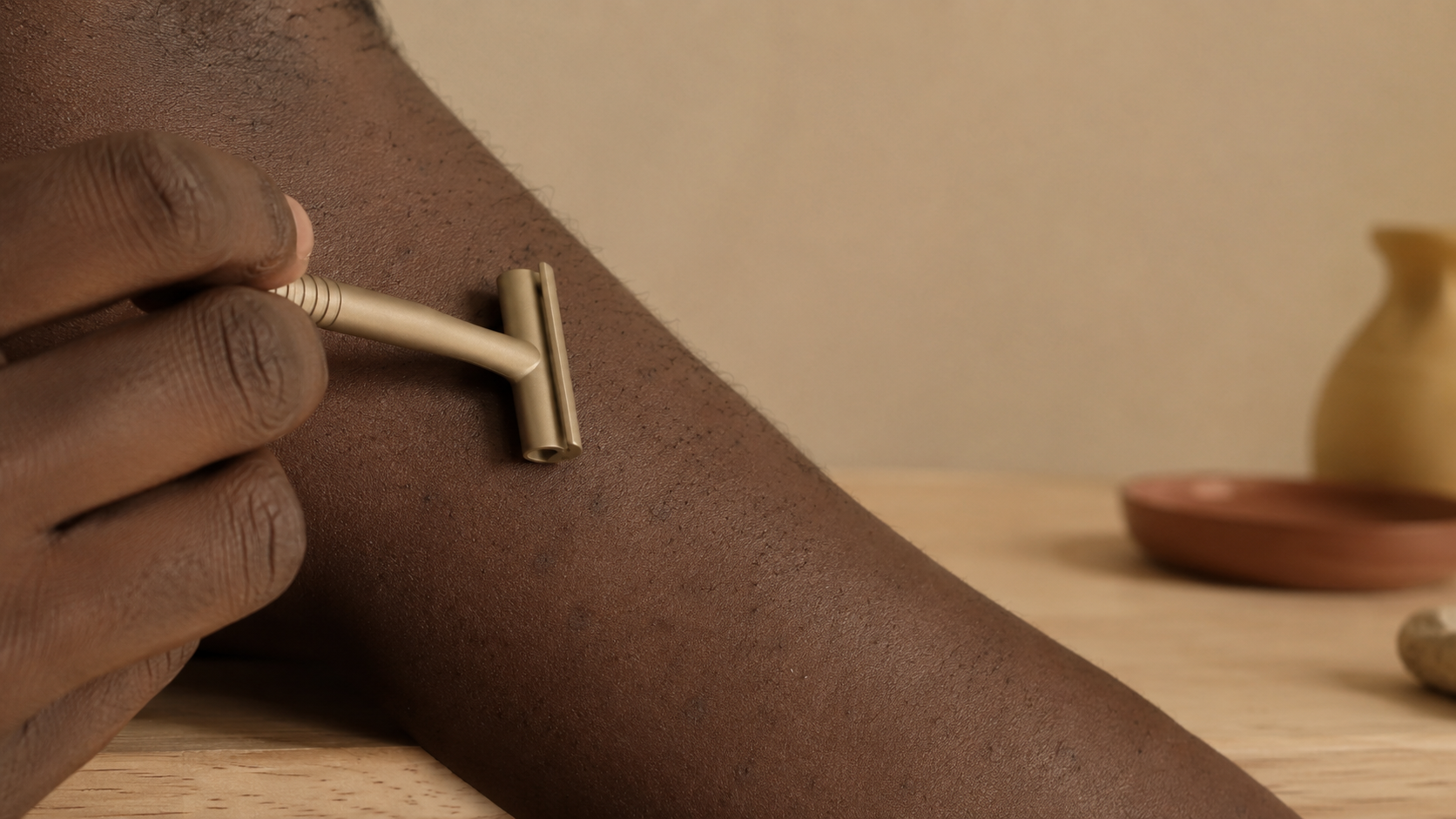 A hand holding a single-blade razor over deep brown skin with razor bumps