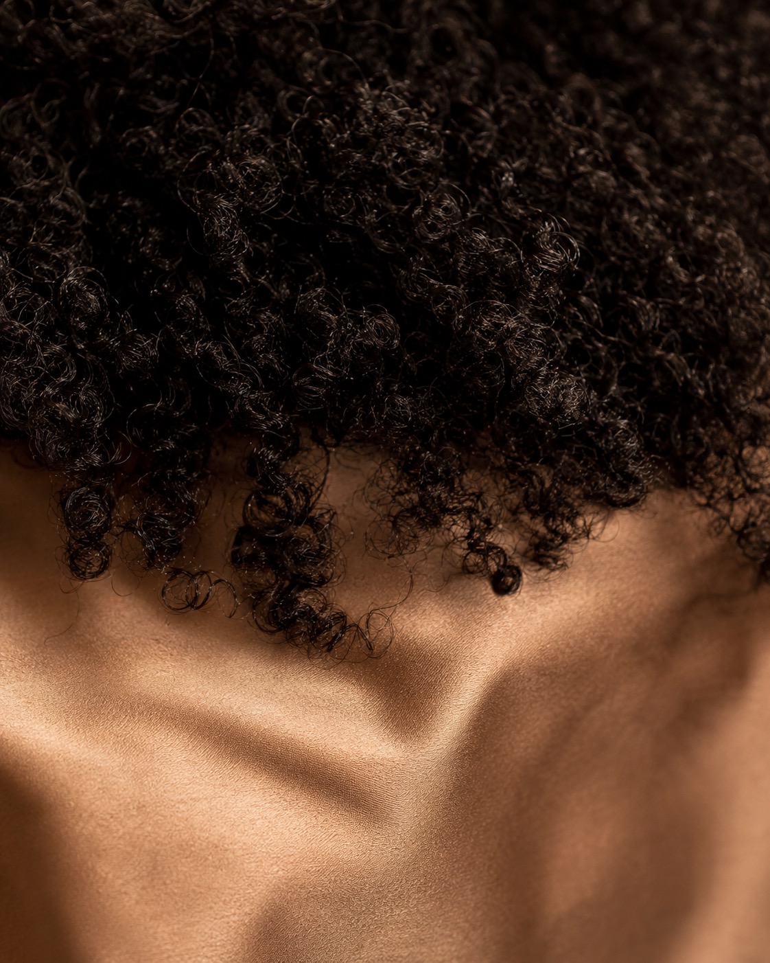 Close detail of tightly coiled hair resting against a silk pillowcase.