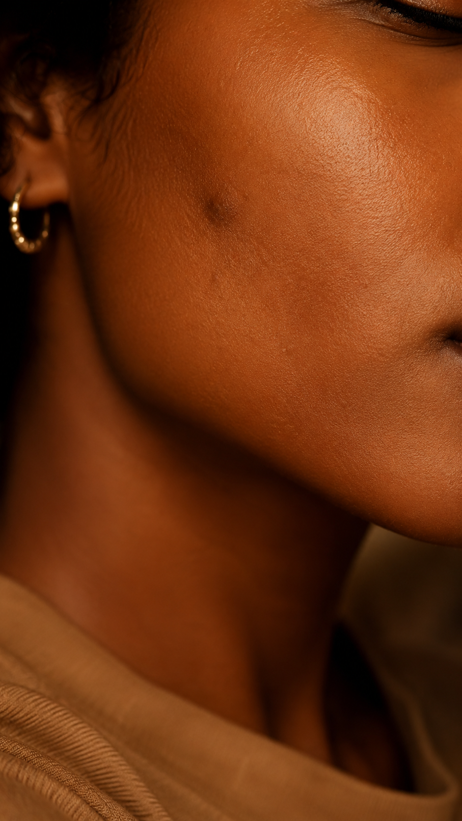 Close view of deep brown skin with a persistent dark mark on the cheek.